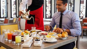 A breakfast setting with various dishes, drinks, and a waiter serving.