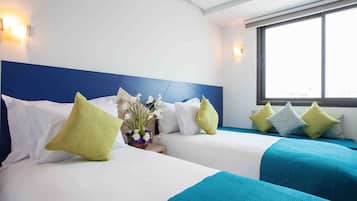 A hotel room with two beds, each with white and blue bedding, and a large window providing a view.