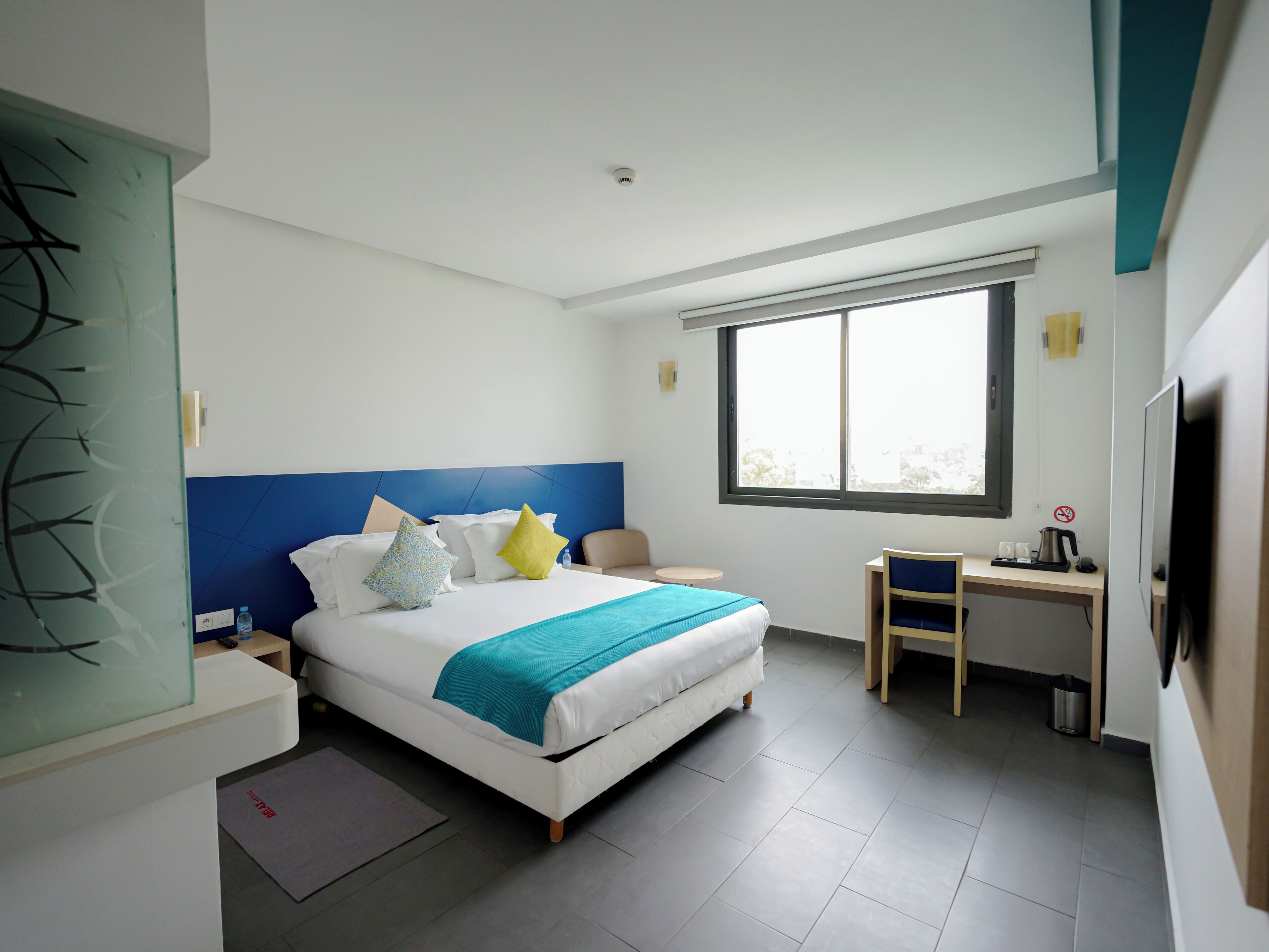 A modern hotel room with a large bed, a desk, and a window.
