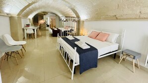 A hotel room with a bed, a desk, a chair, and a small table. There is a staircase leading to another room. - B&B Pietramare (Melendugno)
