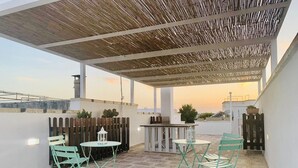 A rooftop patio with a wooden pergola, outdoor seating, and a view of the sunset. - B&B Pietramare (Melendugno)