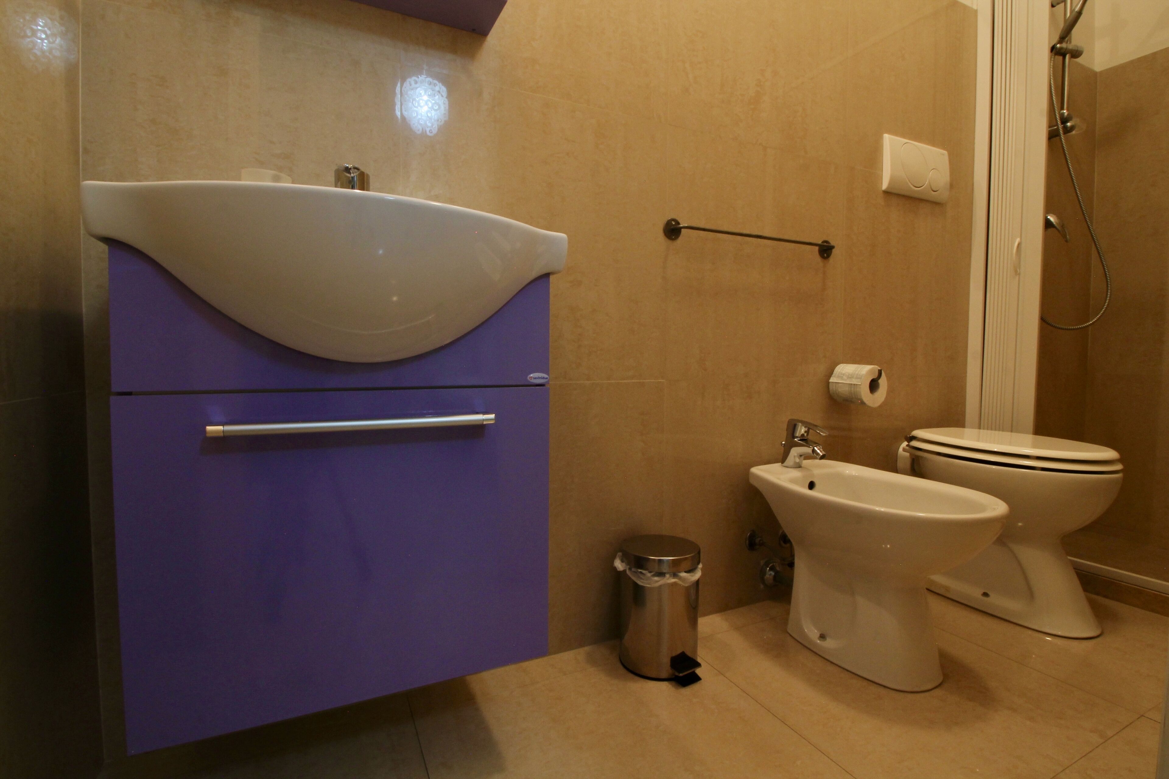 Ein Badezimmer mit einem lilafarbenen Waschtisch, einem Bidet, einer Toilette und einer Dusche.