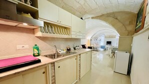 A kitchen with a sink, cabinets, and a countertop. There is a refrigerator and a dining area in the background. - B&B Pietramare (Melendugno)