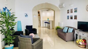 A spacious living area with a sofa, chairs, a TV, and a dining area with a table and chairs. - B&B Pietramare (Melendugno)