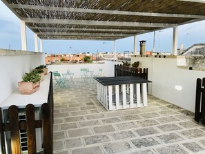 A rooftop terrace with a table and chairs, potted plants, and a pergola. - B&B Pietramare (Melendugno)