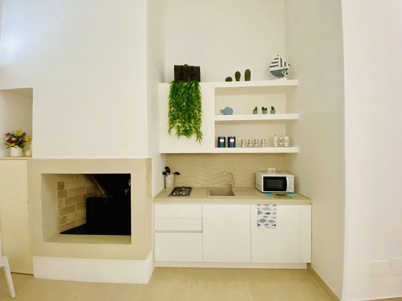 A compact kitchen with a built-in microwave, a small sink, and a shelf with decorative items.