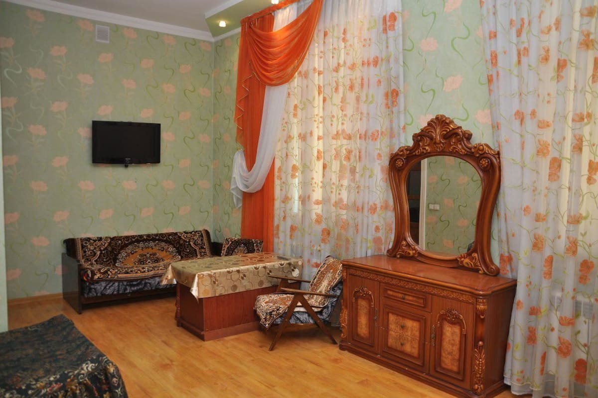 A room with a sofa, a chair, a table, a mirror, and curtains.