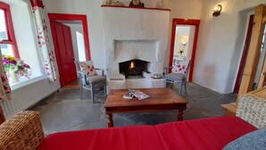 A cozy room with a fireplace, two chairs with floral cushions, a wooden table, and a red sofa. - Teac Chondai Thatched Cottage (Loughanure)