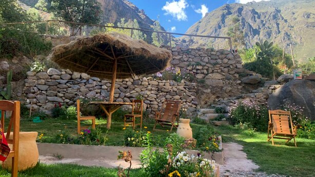 A rustic outdoor seating area with stone walls and a thatched roof structure. - Inka Khawarina Tambo Lodge (Ollantaytambo)