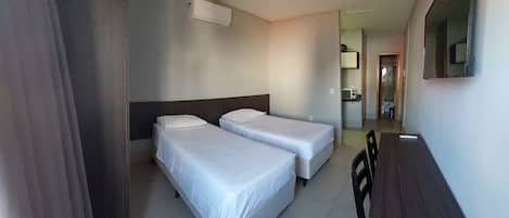 A hotel room with two single beds, a wooden desk, and a mirror on the wall.