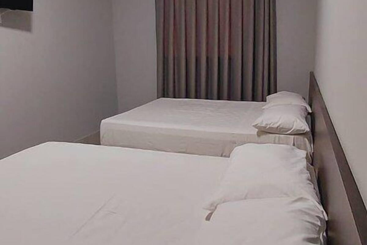 A small, clean room with two beds, a flat-screen TV mounted on the wall, and a window with curtains.