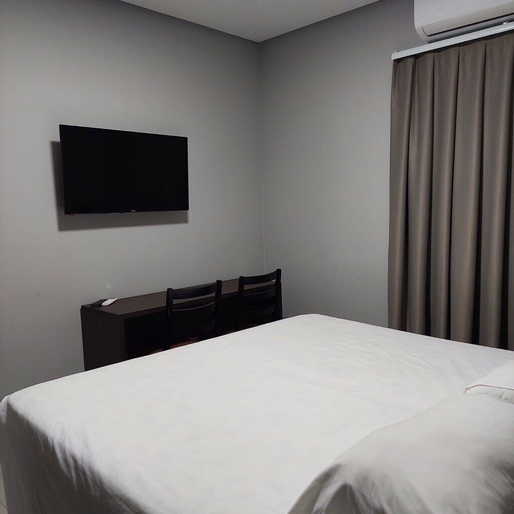 A hotel room with a bed, a desk with chairs, a television, and a window with curtains.
