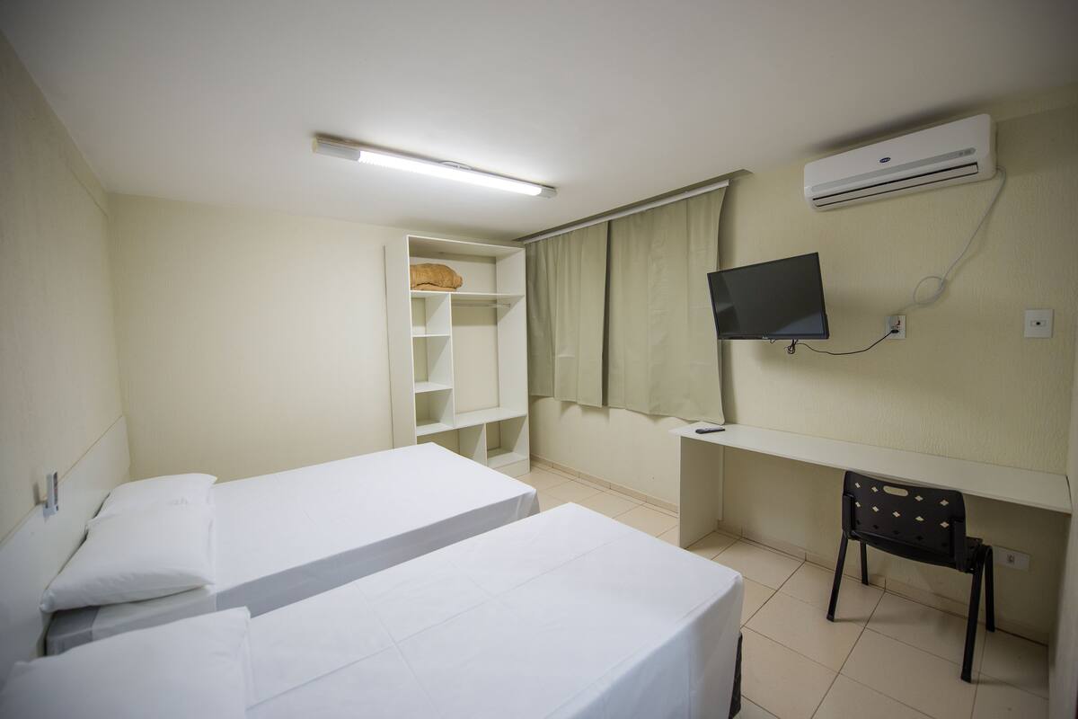 A hotel room with two beds, a TV, an air conditioner, and a desk with a chair.