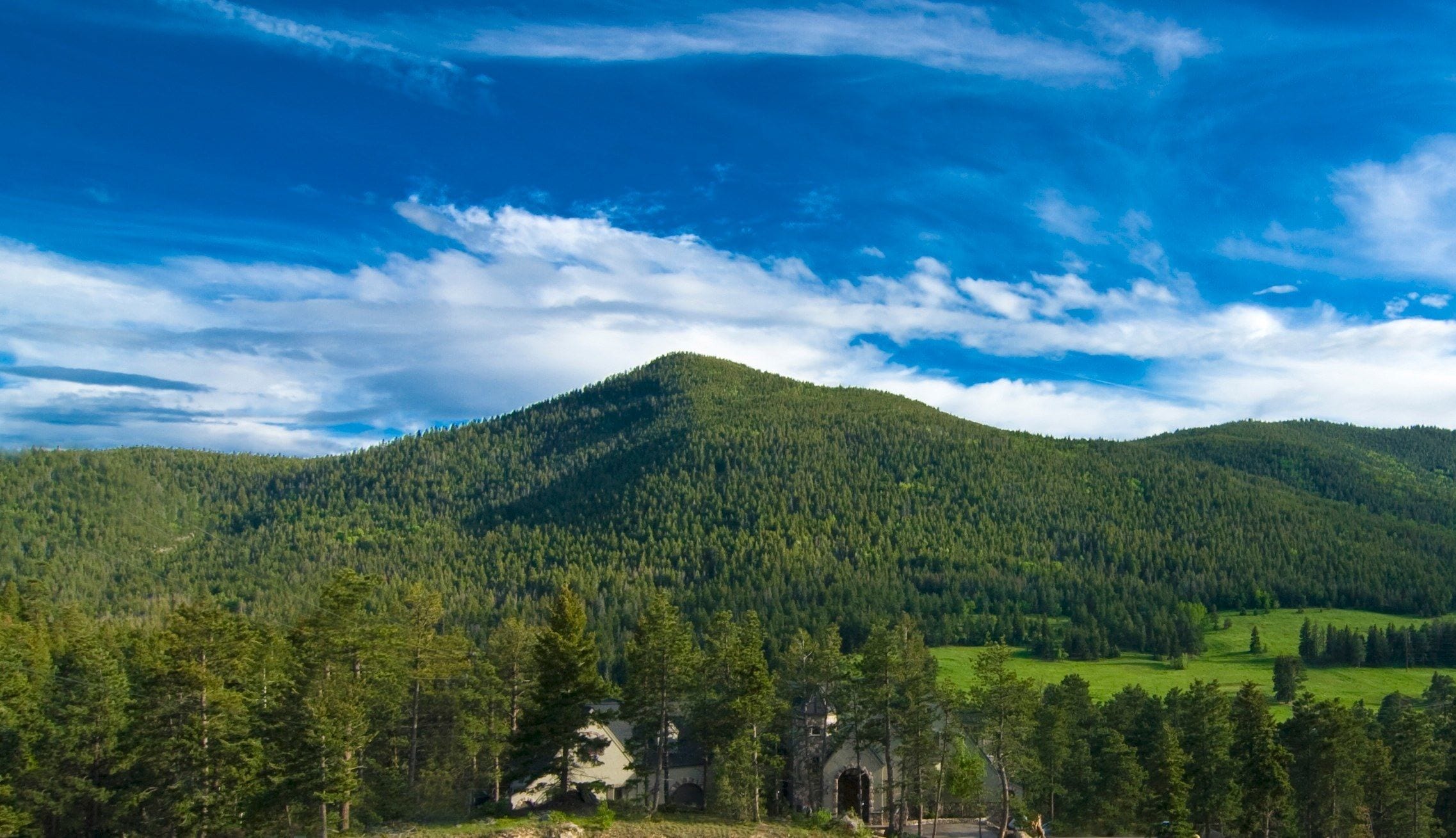 A mountainous landscape with dense forest and a historic stone building with arches.