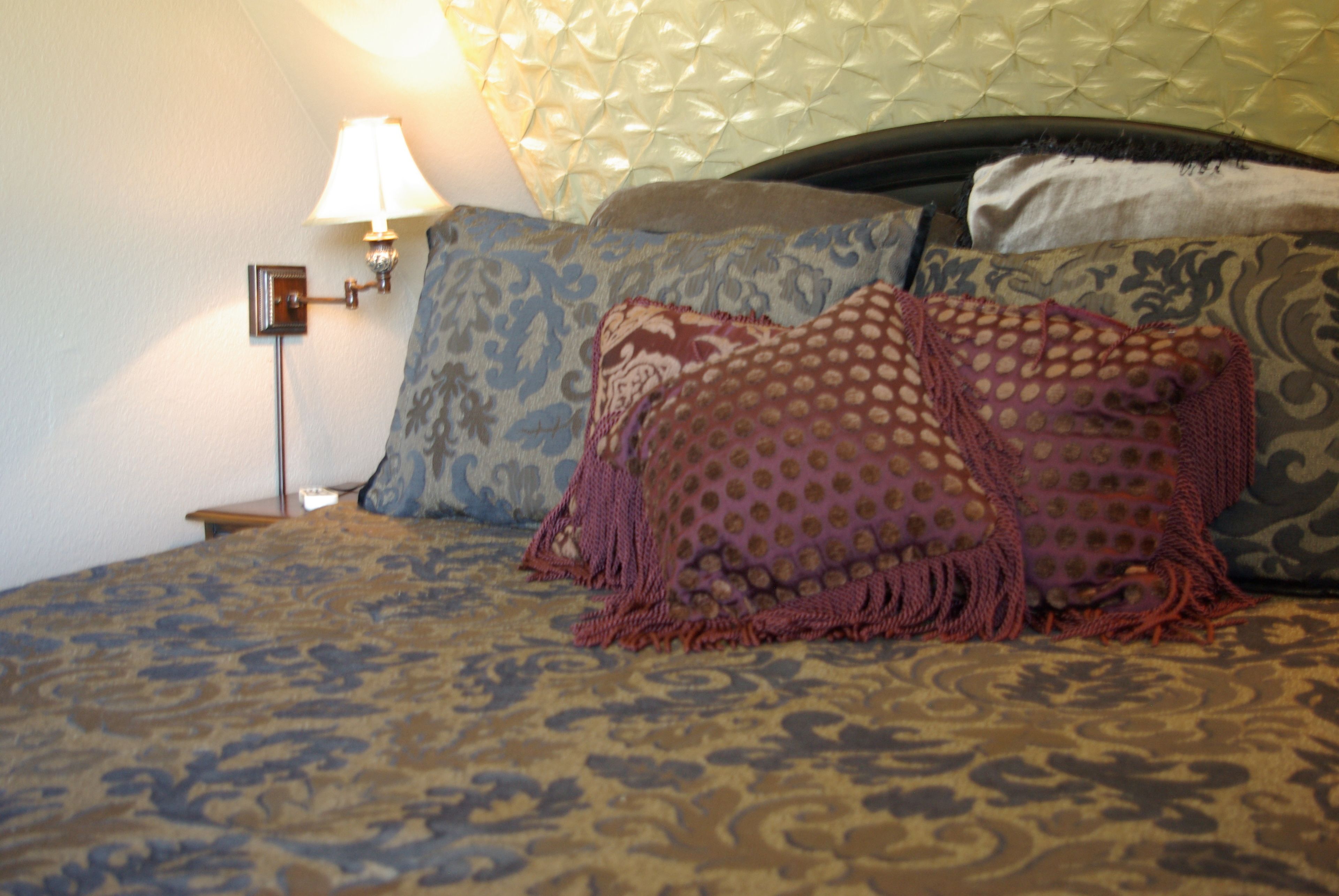 Een slaapkamer met een bed met een patroongedekt laken, meerdere kussens, een bedlamp en een hoofdbord.