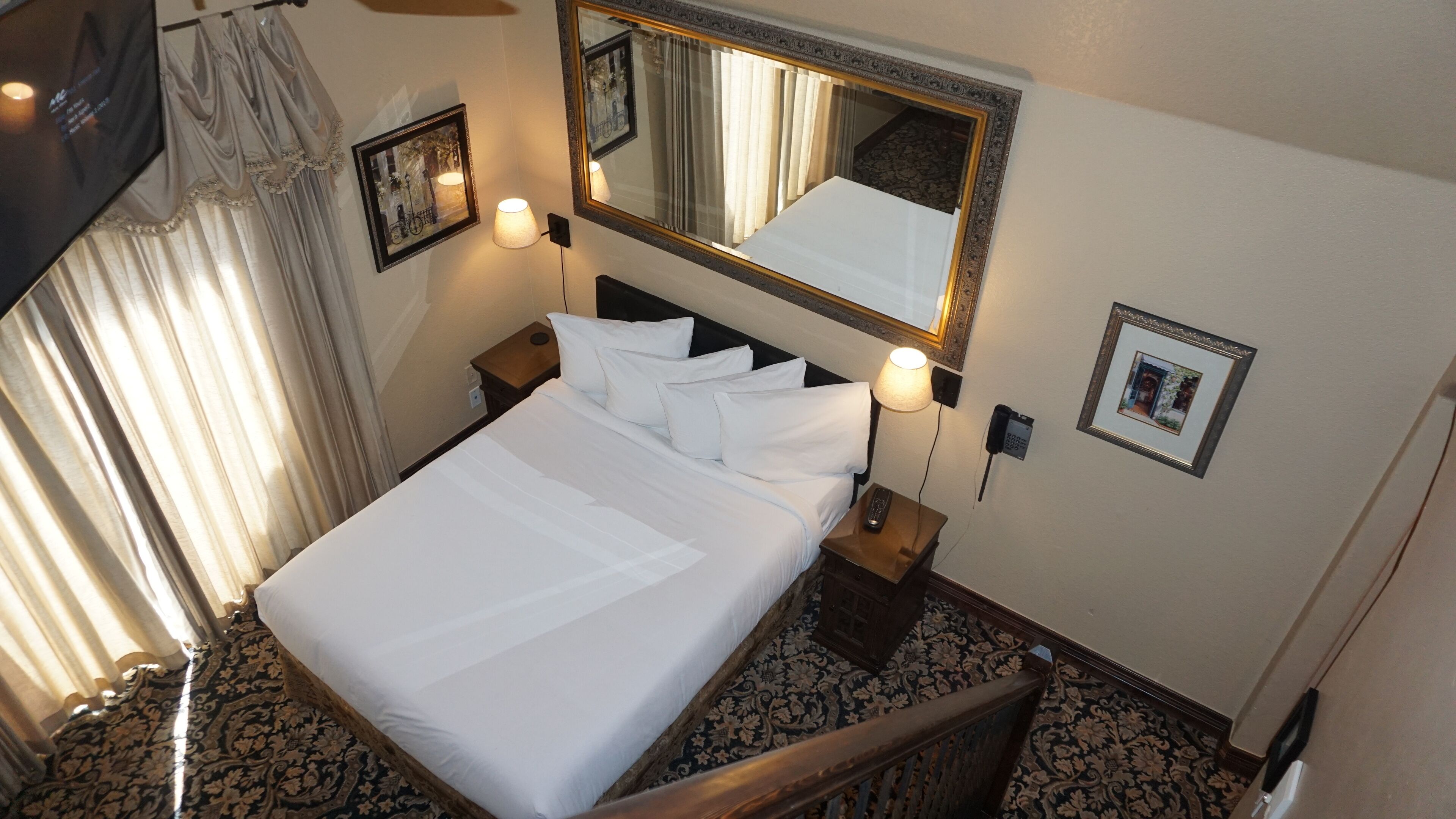 A hotel room with a large bed, a nightstand, a bedside lamp, a telephone, and a mirror on the wall.