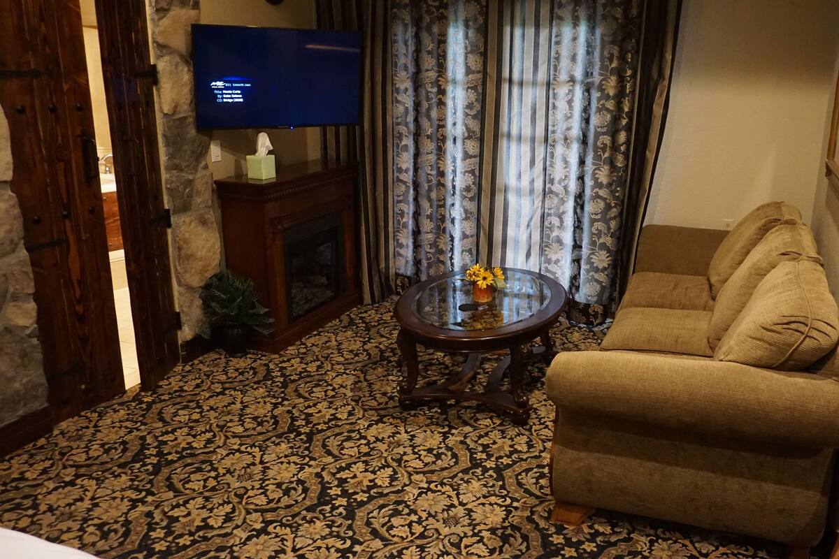 A living room with a sofa, a glass coffee table with flowers, a fireplace, and a television on the wall.