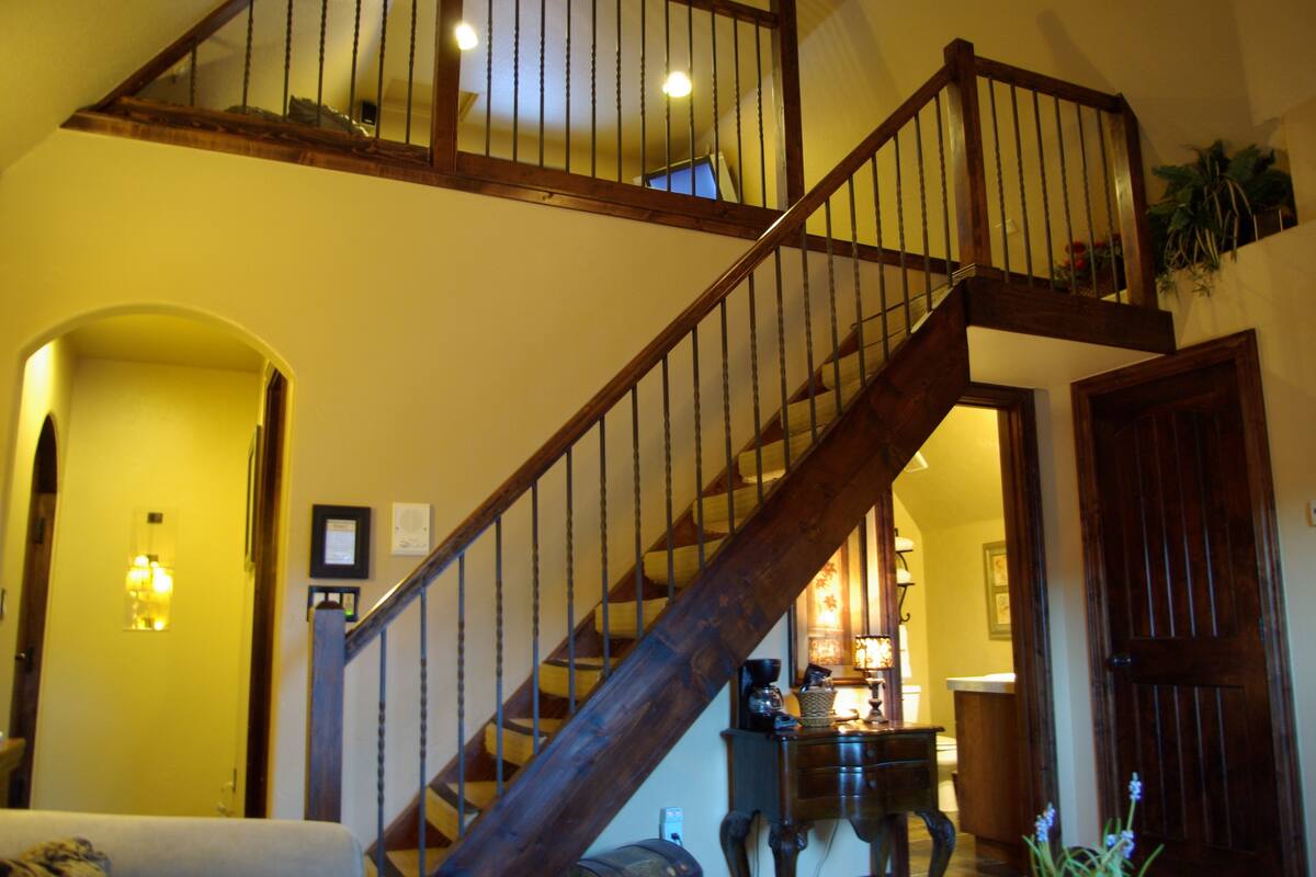 A wooden staircase with a railing, leading to an upper floor. There is a lamp on the landing, and a door is visible to the right.