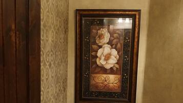 A bathroom with a toilet, a framed floral artwork on the wall, and a patterned wallpaper.