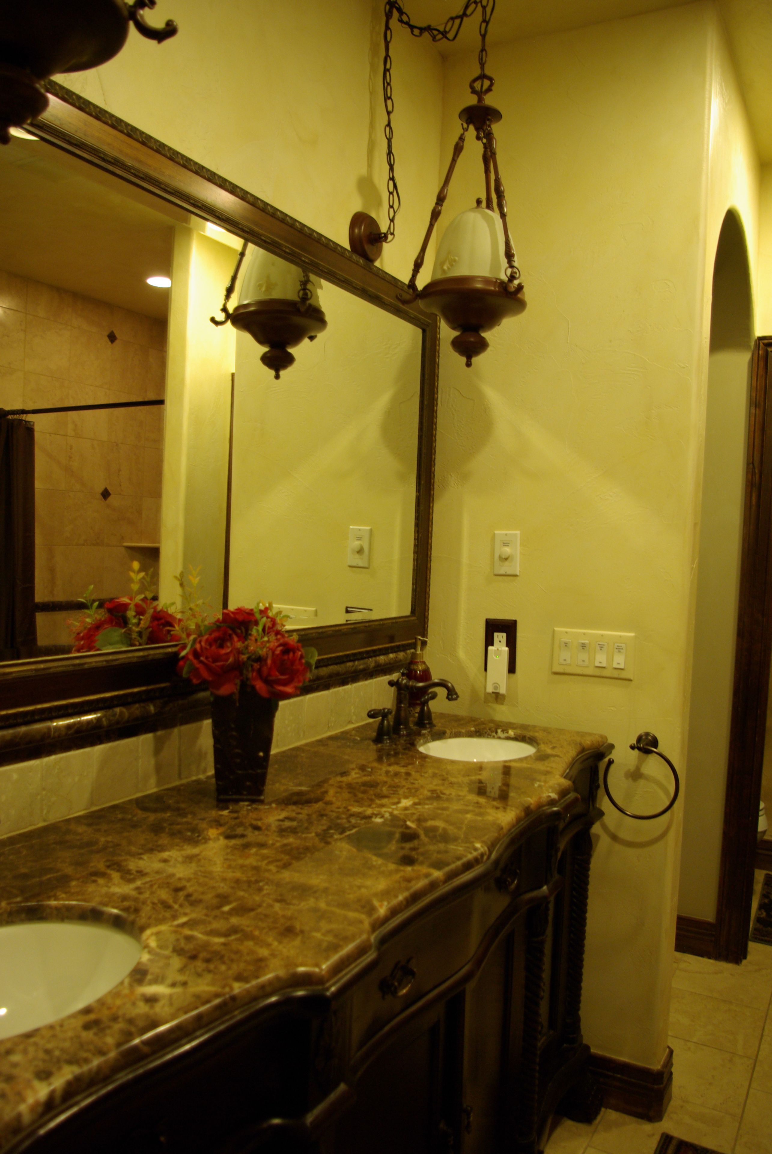 A bathroom with a marble sink, a large mirror, and a vase with red flowers.