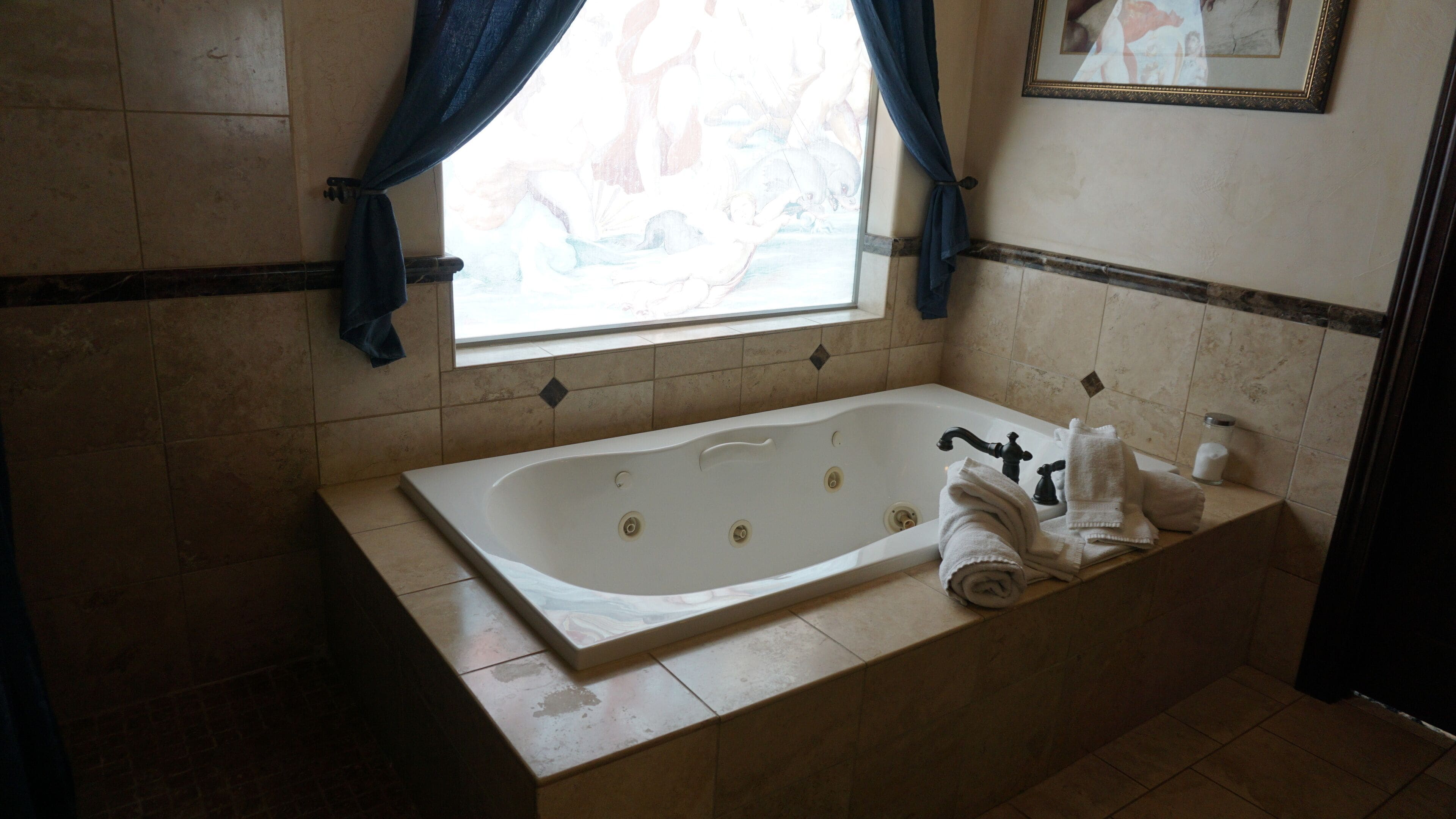 Een badkamer met een groot bad, een raam met gordijnen en een ingelijst schilderij aan de muur.