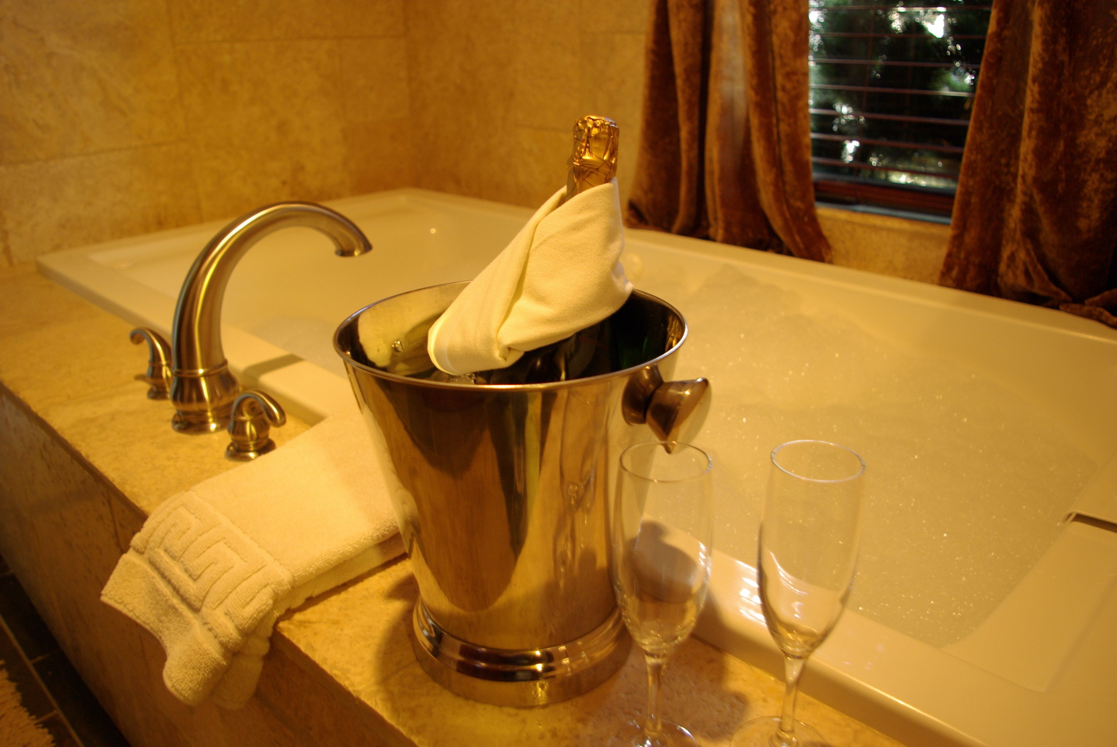Una bañera con una botella de champán y copas, una toalla y un grifo.