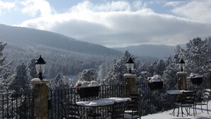 Ein mit Schnee bedeckter Außenbereich mit Steinsäulen und Metallgeländern, mit Blick auf ein bewaldetes Gebirge.