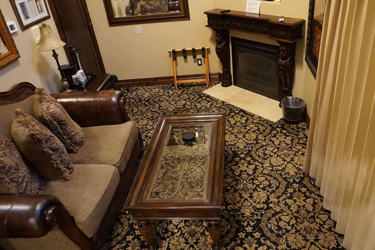 A traditional living room with a patterned carpet, a wooden coffee table, a sofa with patterned cushions, a fireplace, and a small wooden stand.