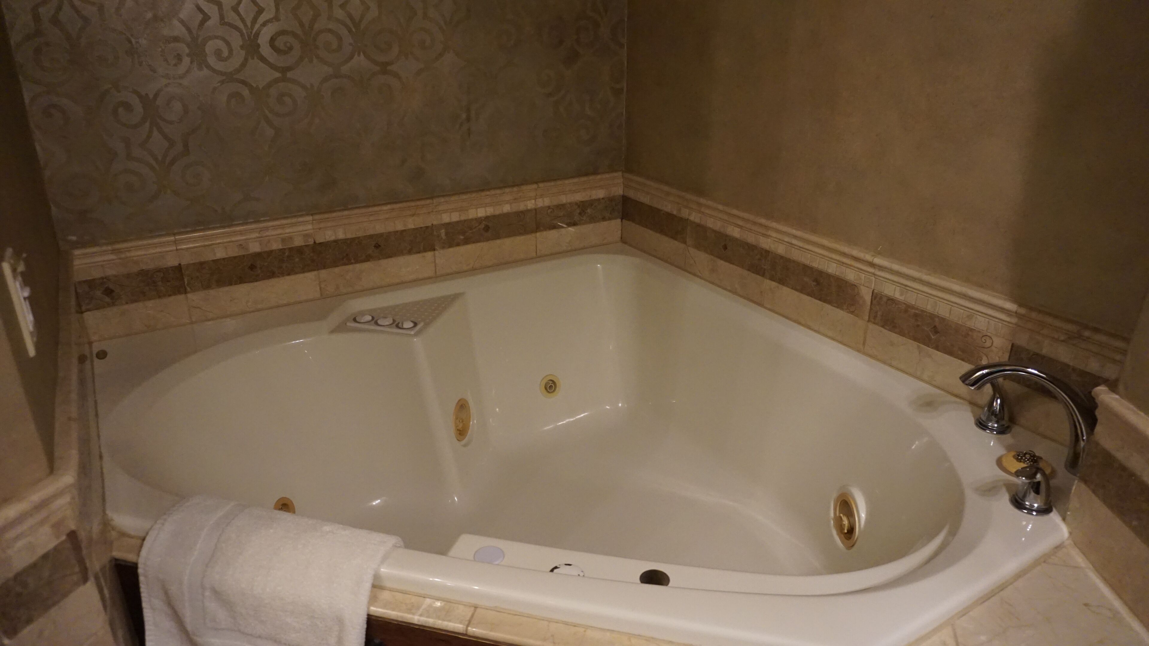 A large, white bathtub with a single faucet and a control panel, set in a bathroom with patterned walls and a tiled floor.