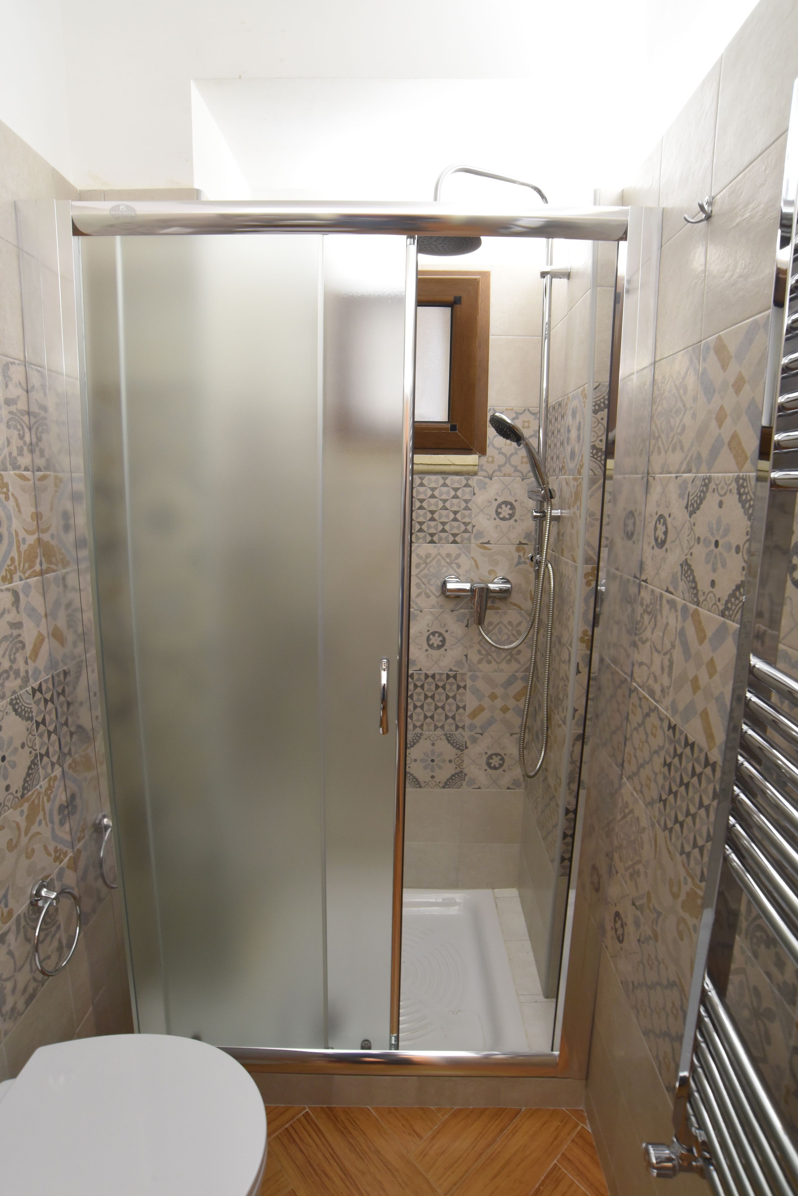 Ein kleines Badezimmer mit Toilette, einer Duschkabine aus Glas und einer gefliesten Duschfläche.