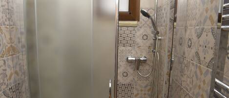 A small bathroom with a toilet, a glass shower enclosure, and a tiled shower area.