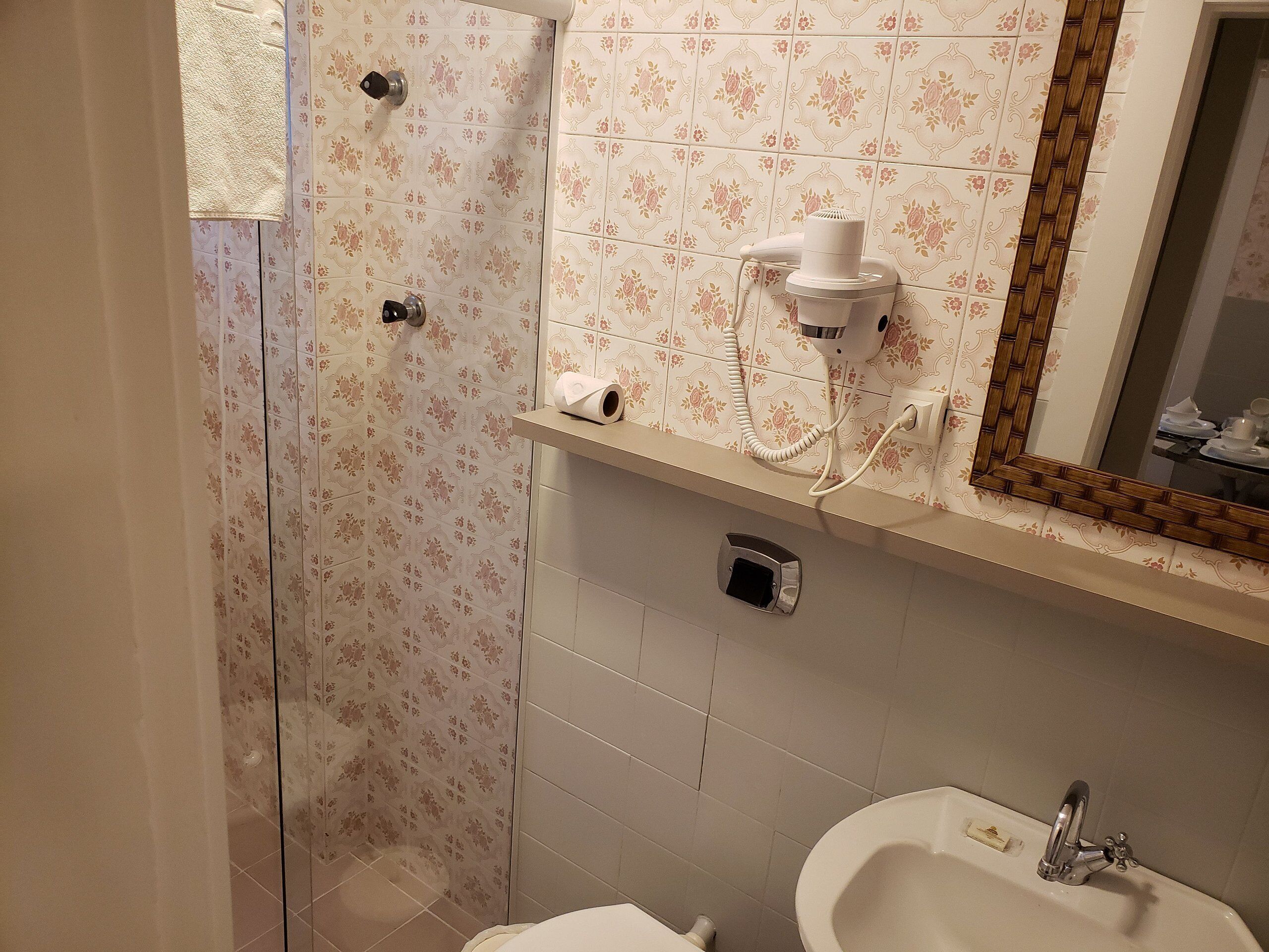 Un baño con ducha, inodoro, lavabo y un espejo con marco decorativo.