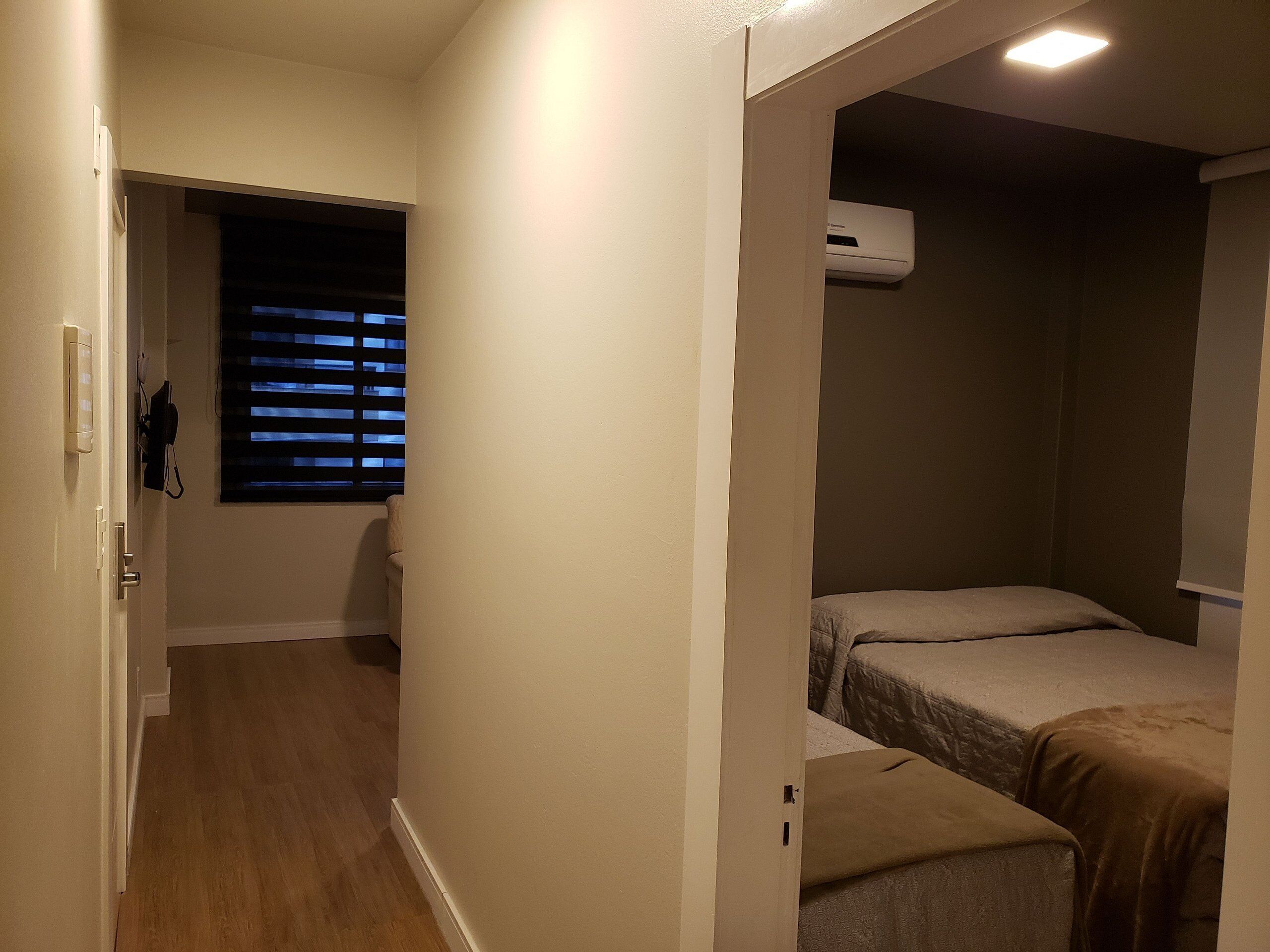 A narrow hallway with a door leading to a room with two beds and an air conditioning unit.
