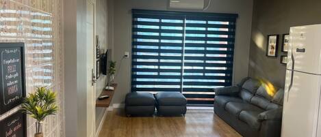 Una sala de estar moderna con un sofá, una mesa de comedor con platos y tazas, un accesorio de iluminación decorativo y un refrigerador.