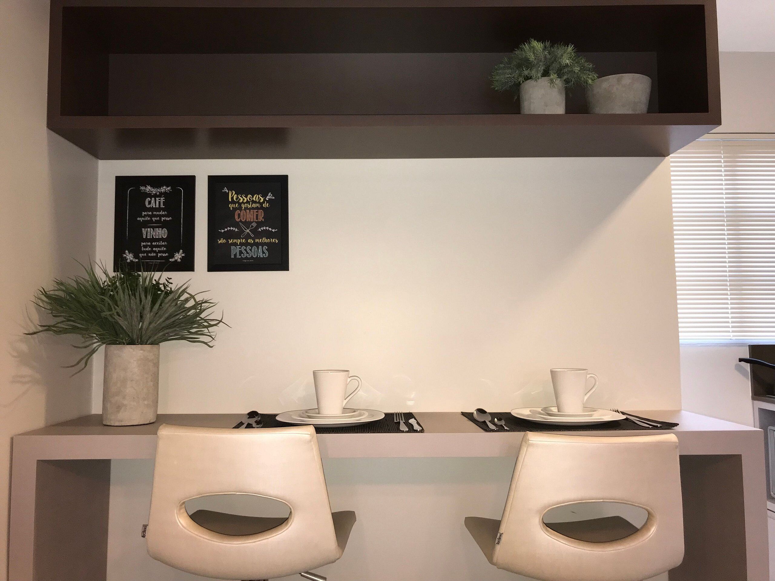 A modern dining area with two chairs, a table set for two, and two framed quotes on the wall.