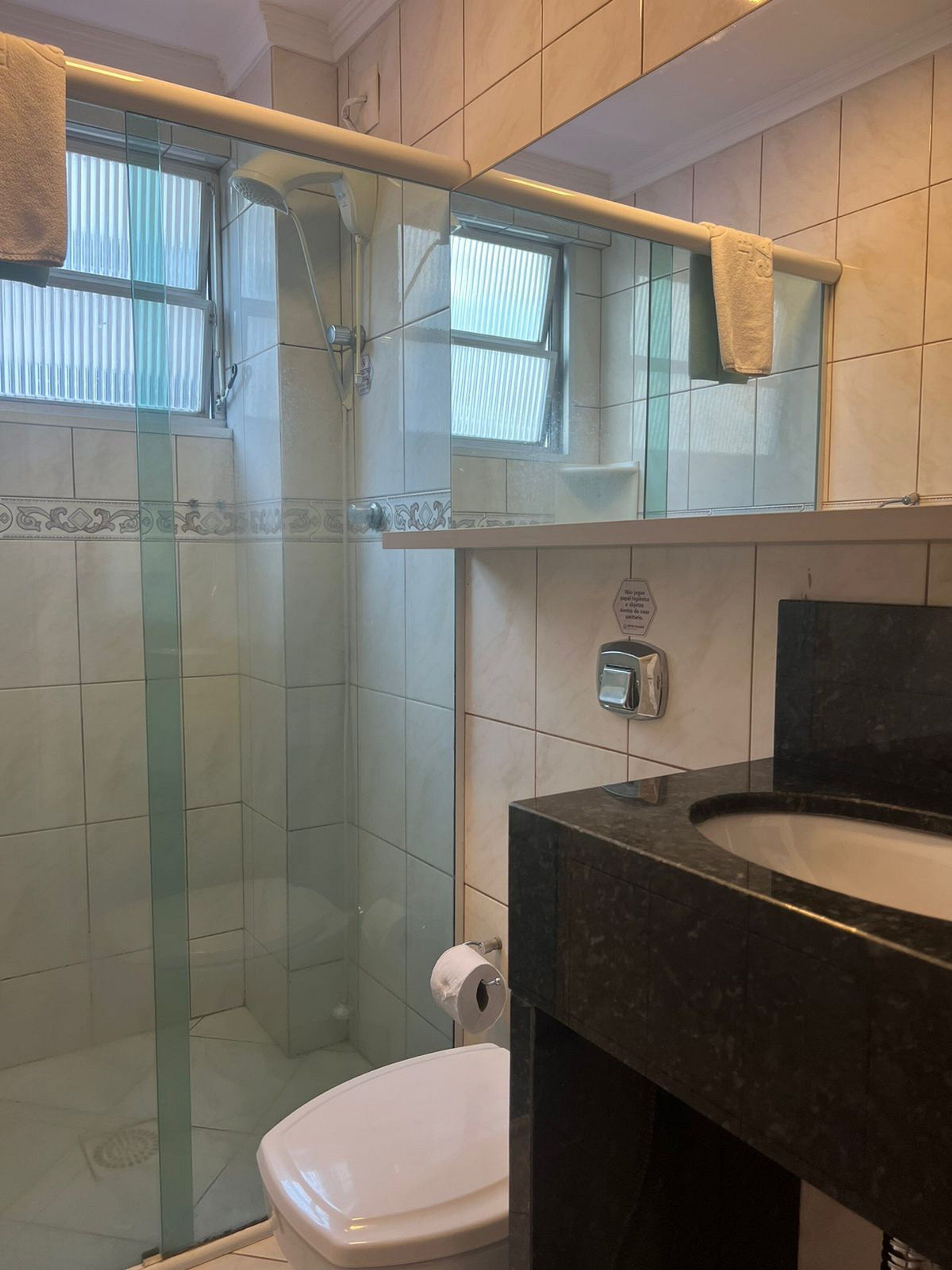 A bathroom with a glass-enclosed shower, a white toilet, and a dark marble sink.