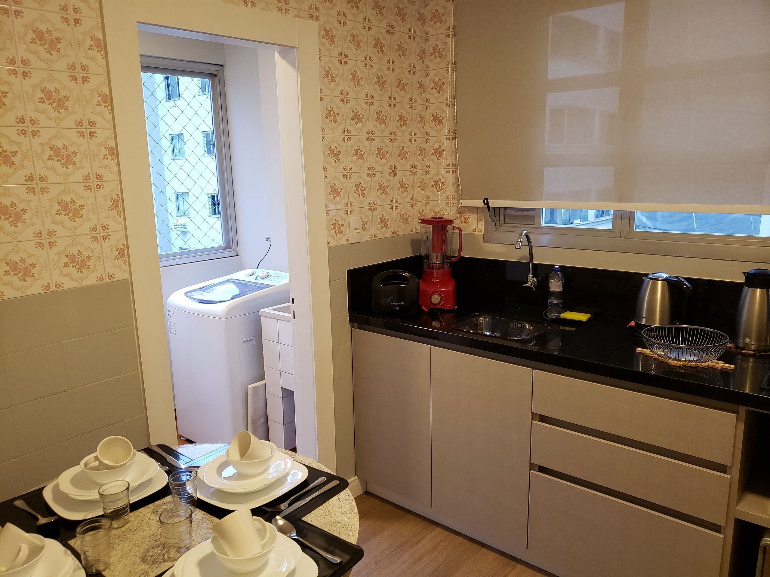 Una cocina compacta con lavadora, una licuadora roja, un hervidor y un lavabo.