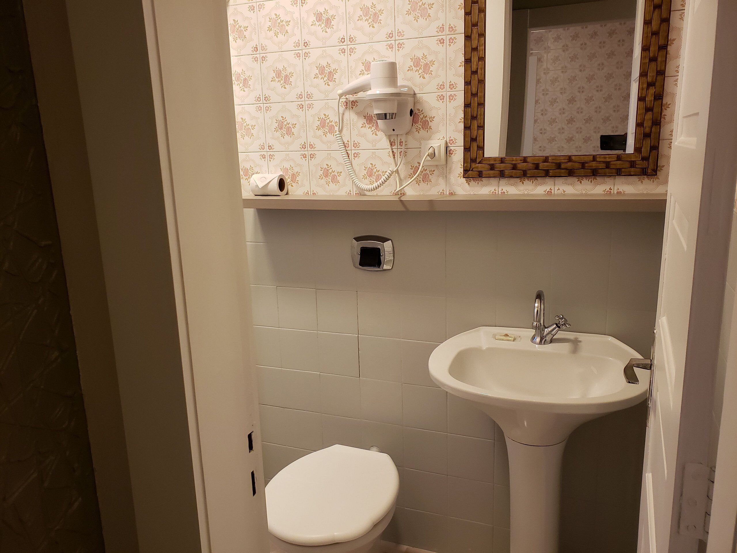 Een badkamer met toilet, wastafel en een haardroger aan de muur.