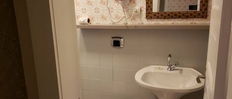 A bathroom with a toilet, sink, and a hairdryer on the wall.