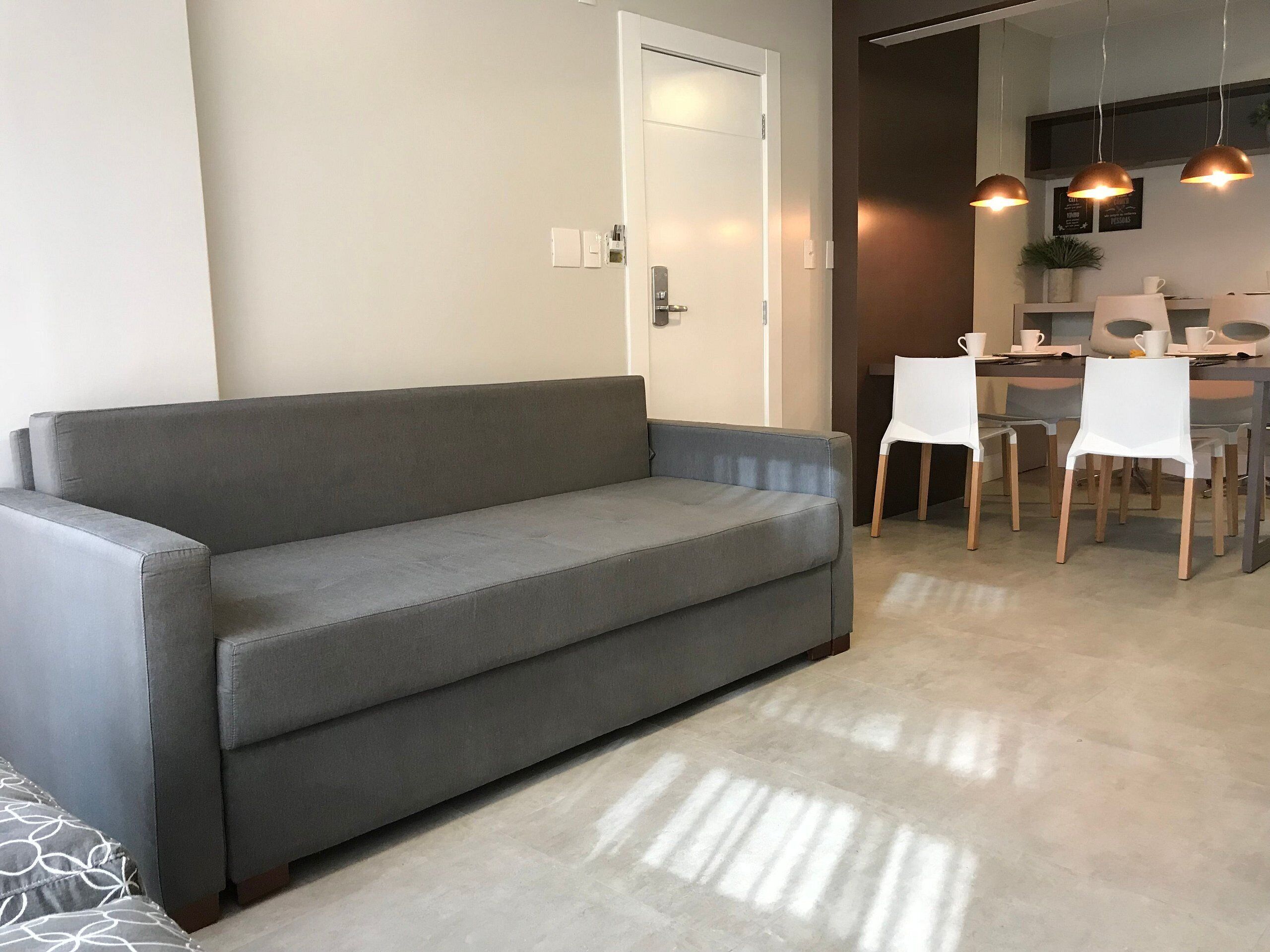 A living area with a grey sofa, a dining table with chairs, and pendant lights.