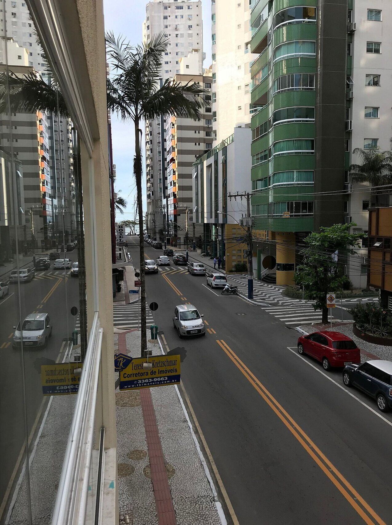 A street view with cars, palm trees, and multi-story buildings.