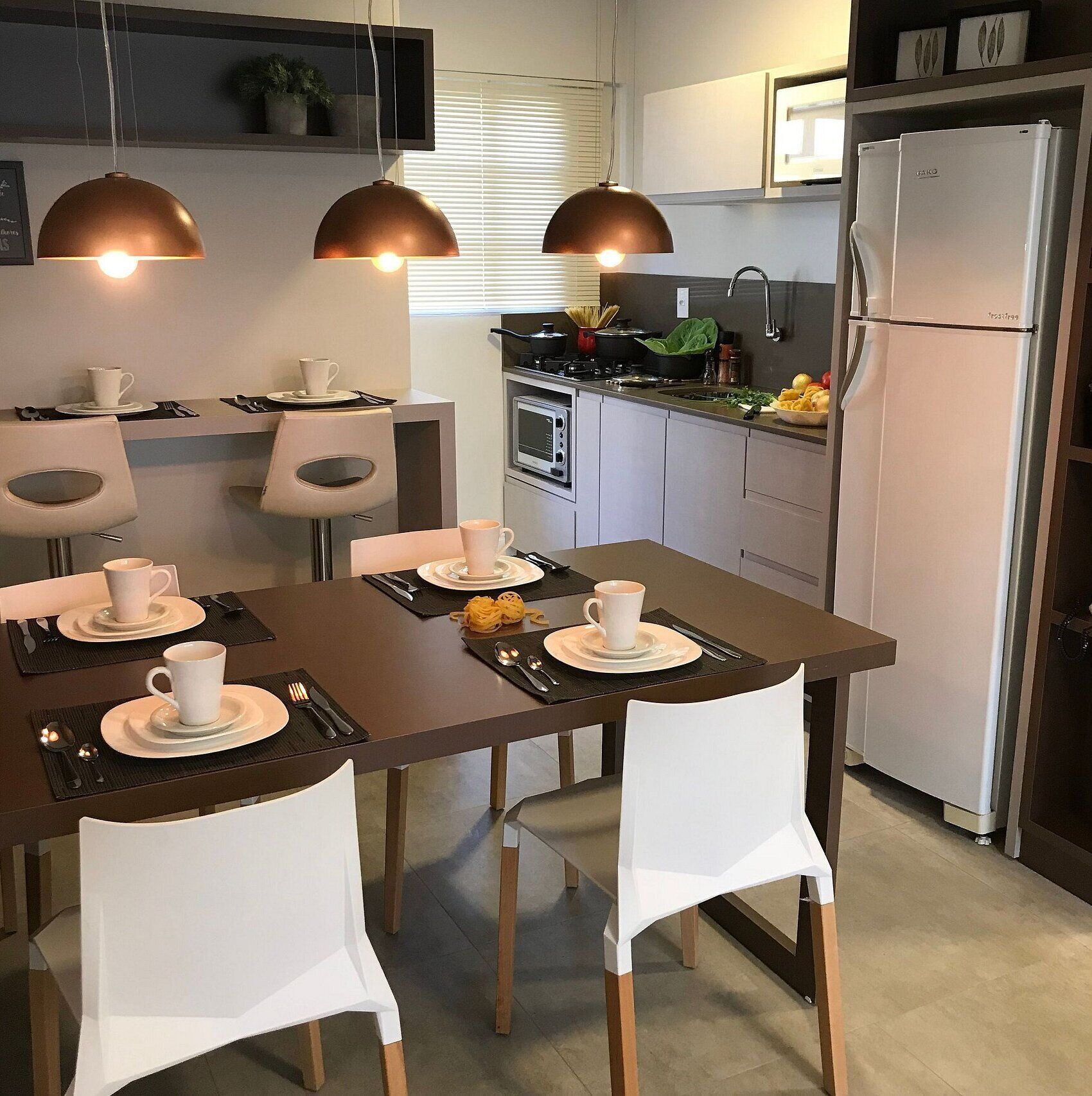 A modern kitchen with a dining area, featuring a table set for four, a refrigerator, and pendant lighting.