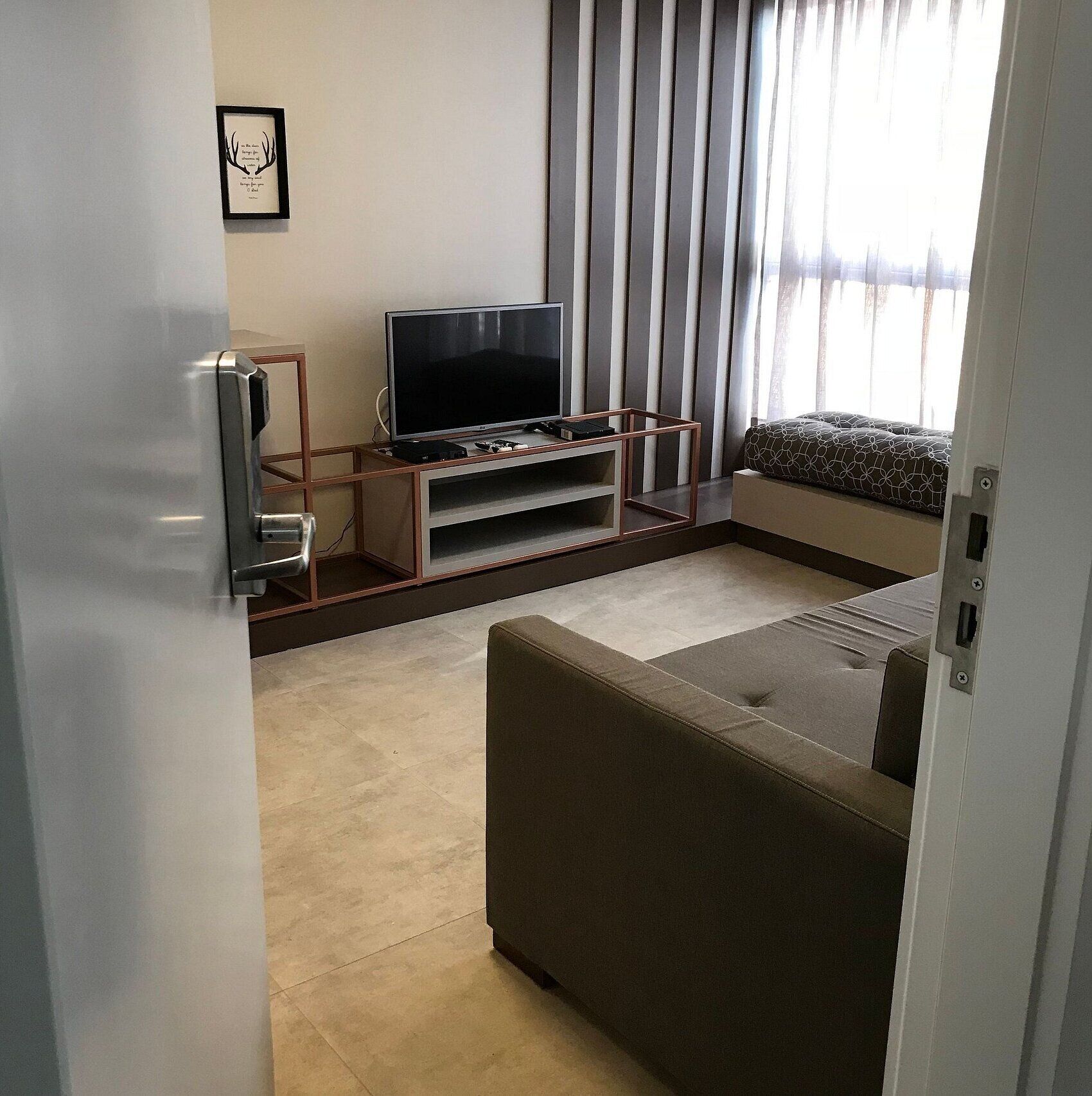 A modern living room with a flat-screen TV on a wooden stand, a sofa, and a patterned cushion.