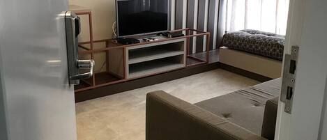 A modern living room with a flat-screen TV on a wooden stand, a sofa, and a patterned cushion.