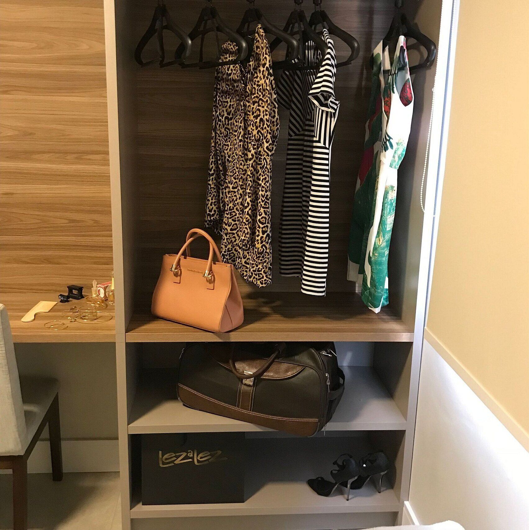 A closet with hanging clothes, a handbag, and shoes on shelves.