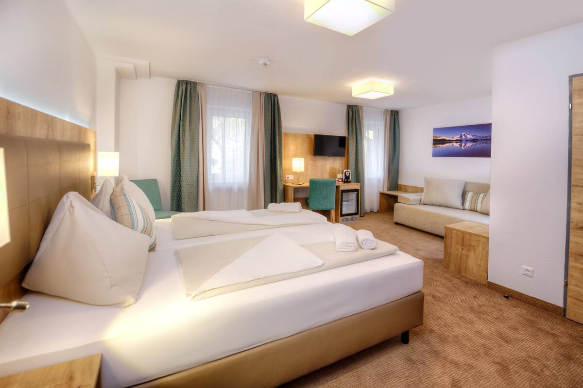 A hotel room with a large bed, a sofa, a desk, and a TV.