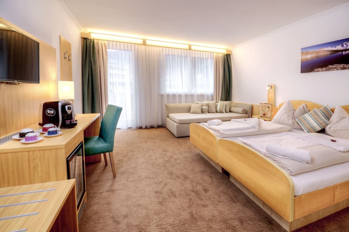 A hotel room with a bed, a sofa, a desk with a coffee maker, and a TV.