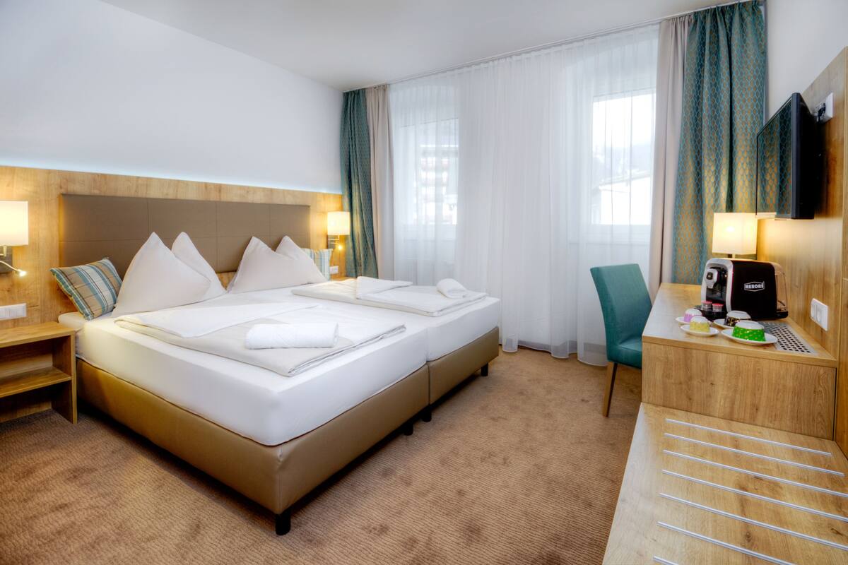 A hotel room with a large bed, a desk with a coffee maker, a chair, and a TV.