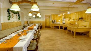 A long dining table with white tablecloths and orange runners, wooden benches, and hanging lamps.