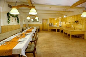 Un lungo tavolo da pranzo con tovaglie bianche e runner arancioni, panche di legno e lampade a sospensione.